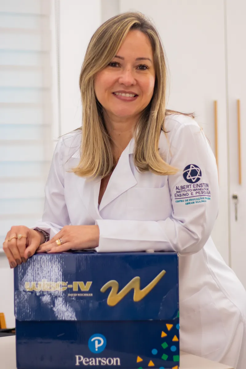 Raquel de jaleco apoiada no kit de testes WISC-IV, usado na avaliação neuropsicológica